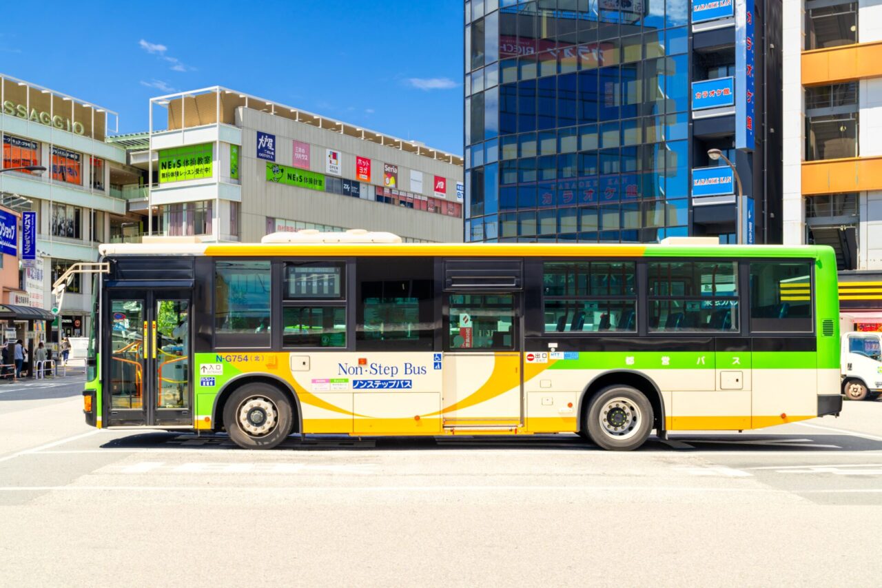 Side view of a green and yellow Toei local bus in Tokyo showing front and center doors