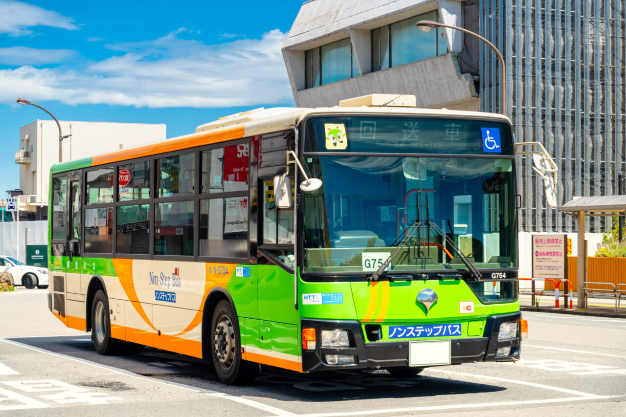 Green and orange low-floor local bus on a city street in Japan