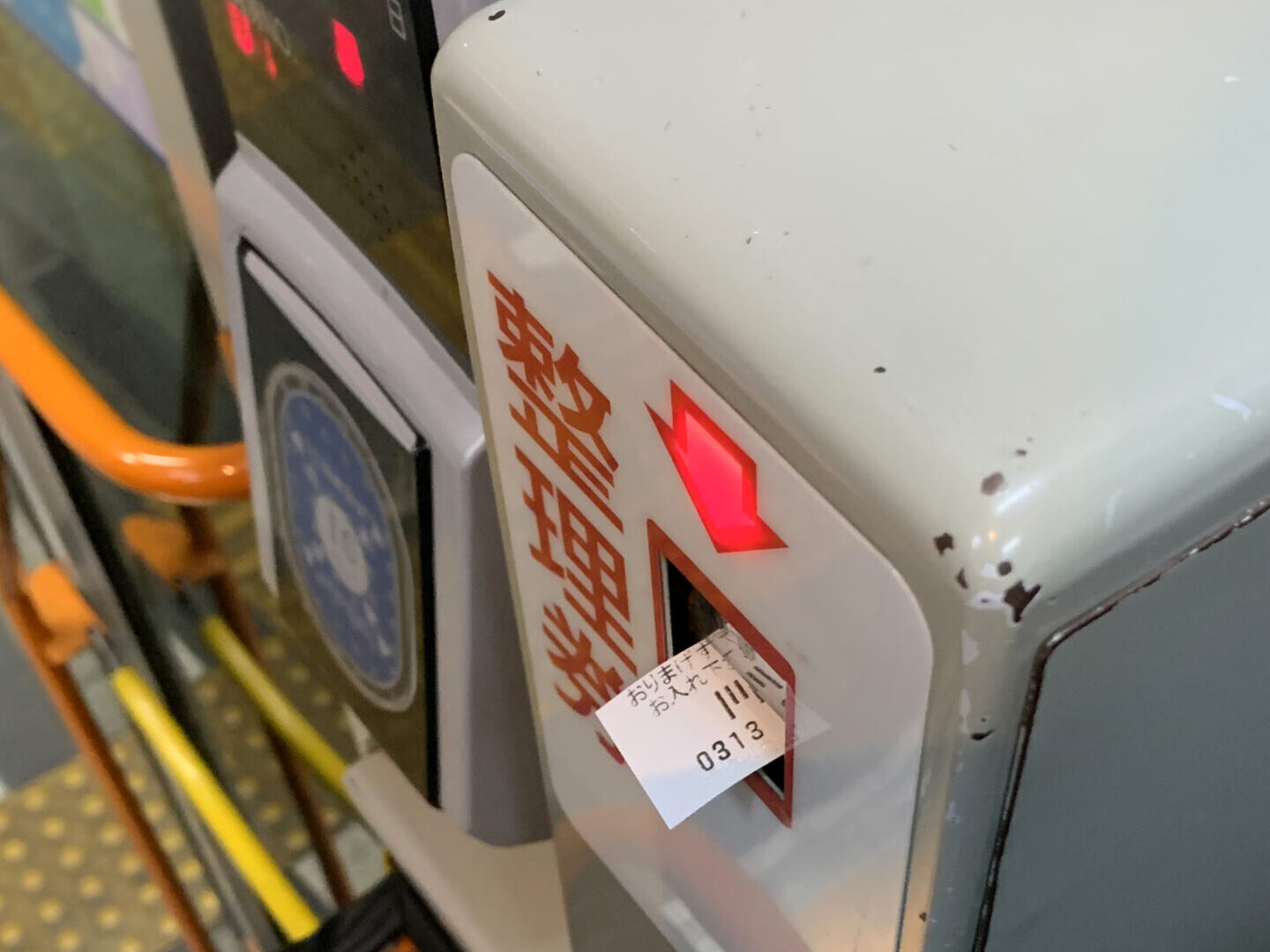 Numbered-ticket dispenser inside a Japanese local bus with a paper ticket protruding